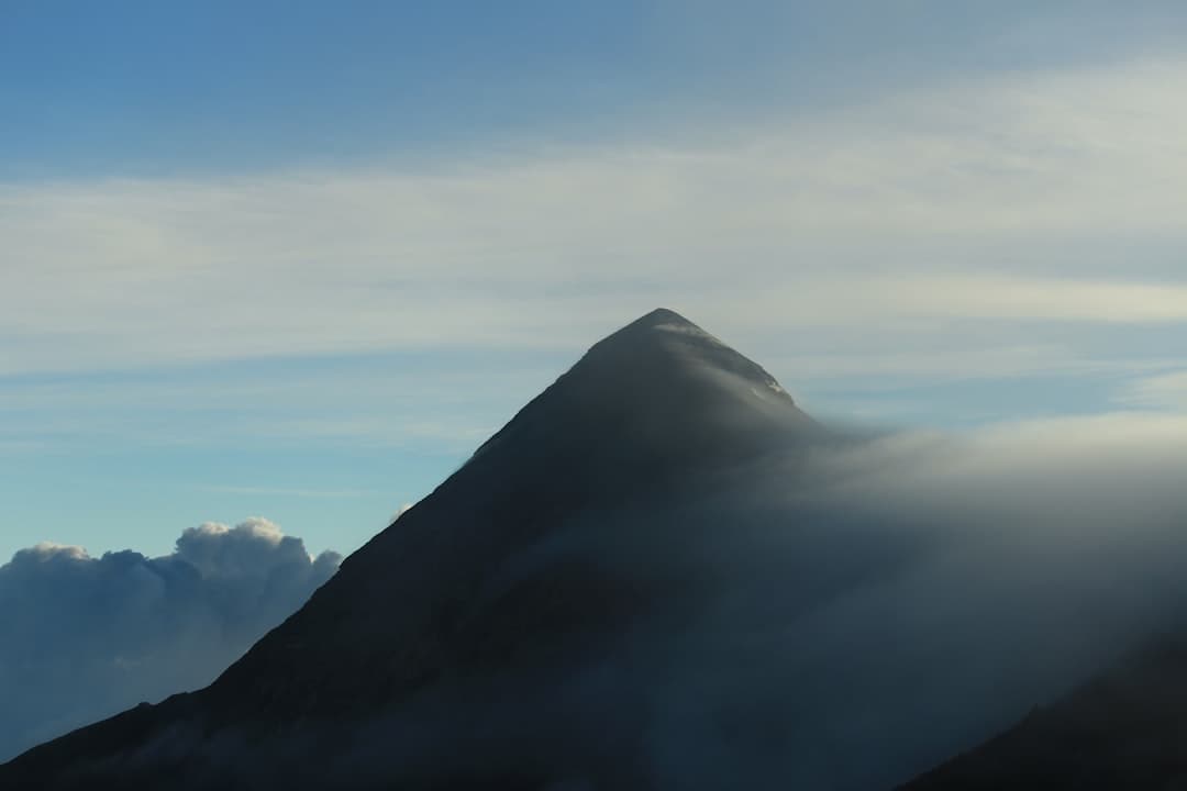 a very tall mountain covered in clouds under a blue sky