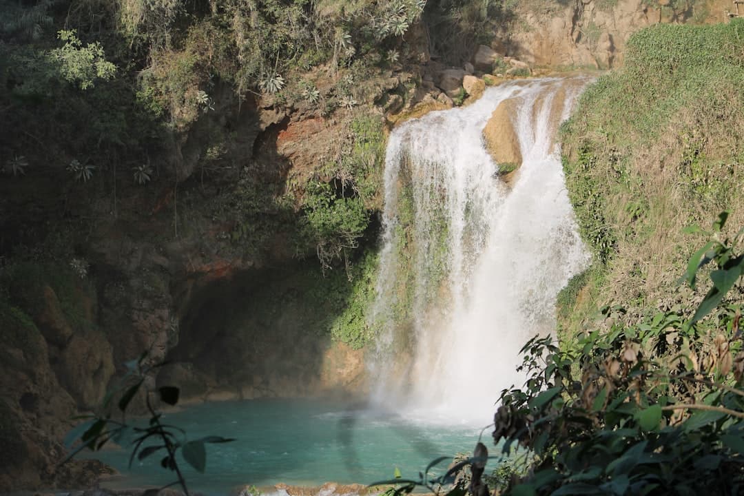 a waterfall with a man standing at the bottom of it